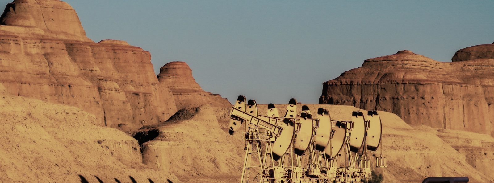 A row of pumpjacks working beneath eroded badland cliffs